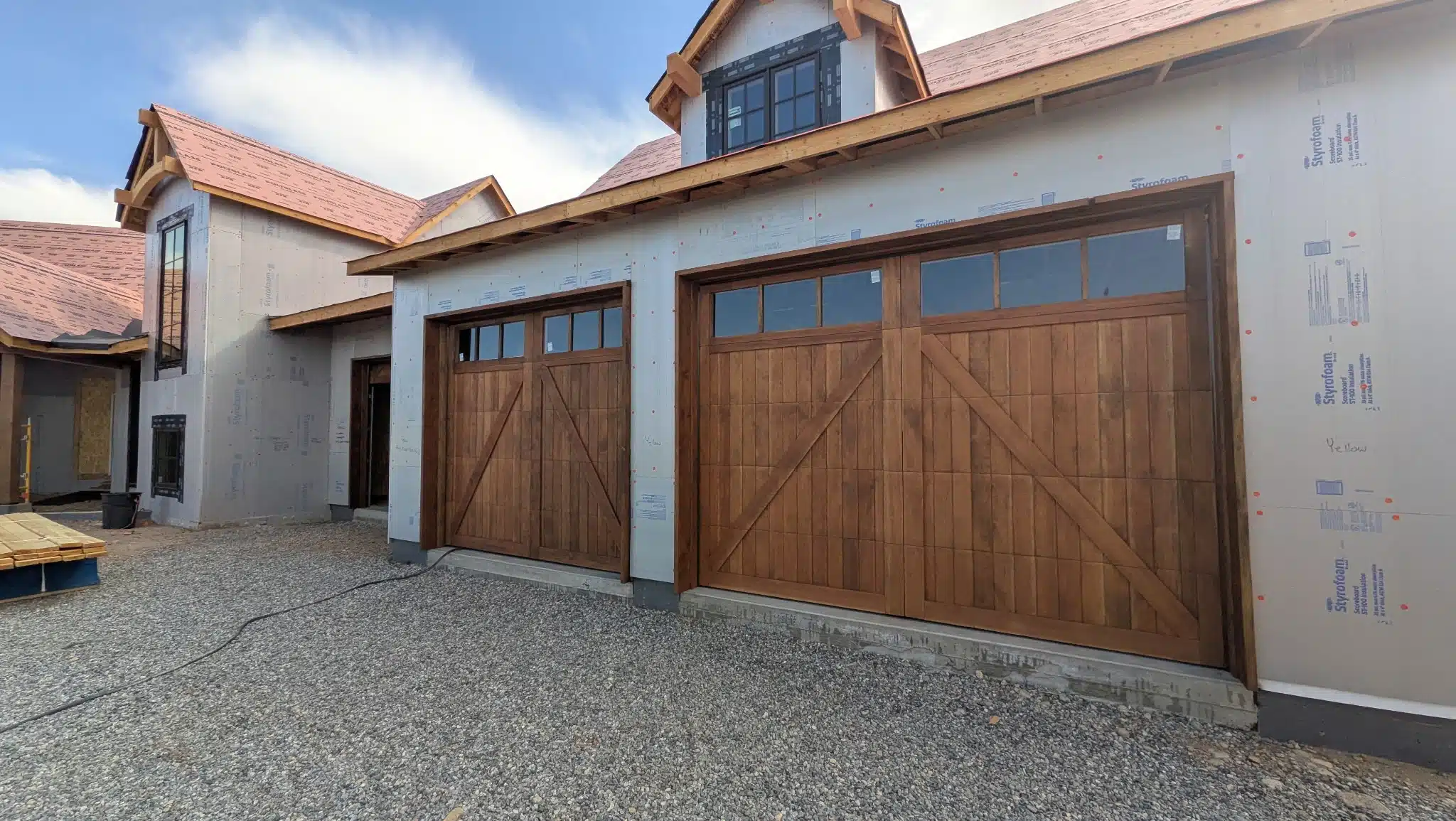 Professional Wood Garage Door Staining for New Construction Two beautifully stained wooden garage doors on a new construction home, enhancing the exterior appeal.