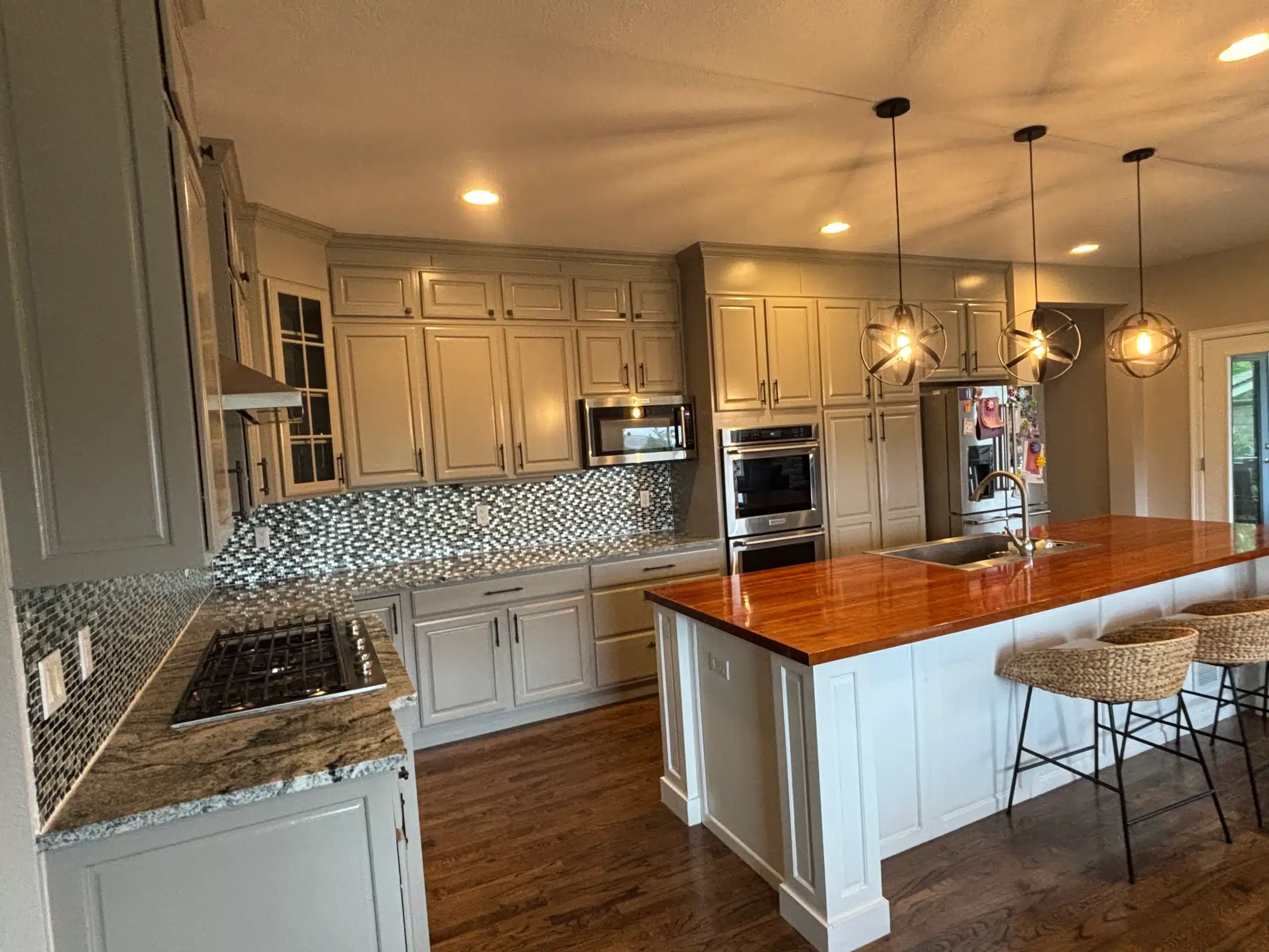 Kitchen Cabinet Painting and Wood Island Staining Project A modern kitchen featuring light gray painted cabinets, a mosaic backsplash, and a rich wood stained island countertop.