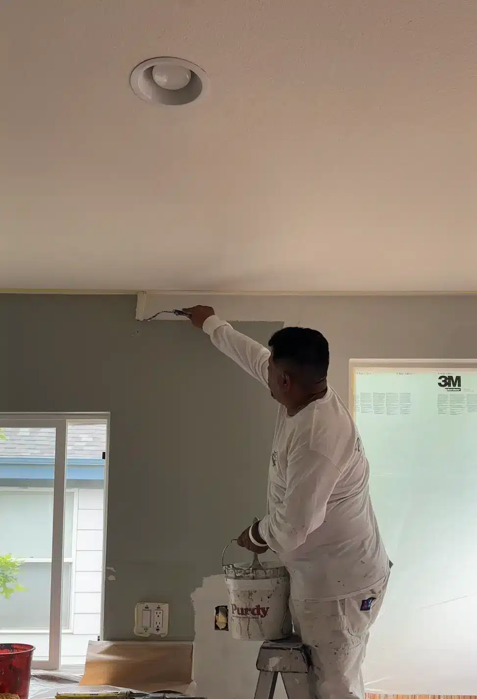 Professional Painter Cutting In Ceiling Line A professional painter meticulously cutting in a clean ceiling line with a brush and gray paint during an interior house painting project.