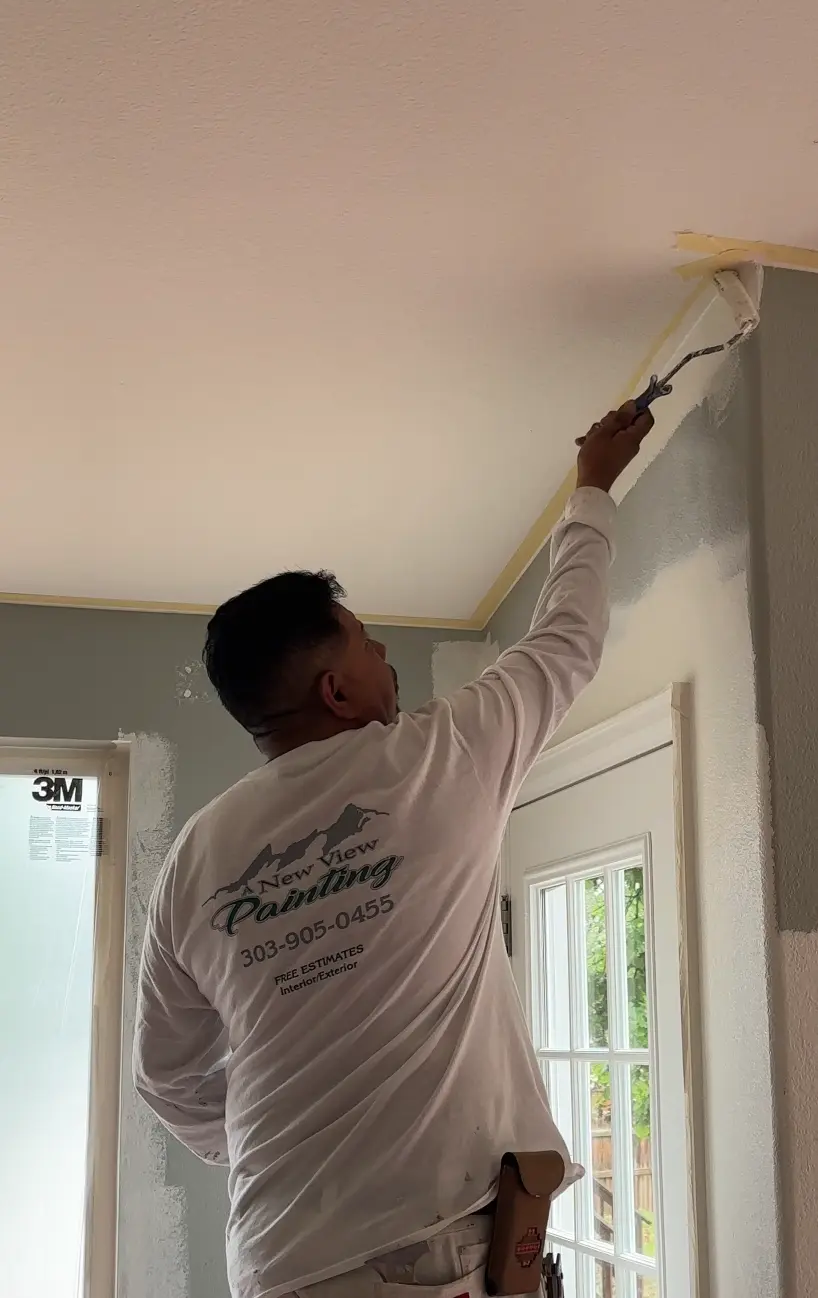 Expert Painter Applying Wall Paint Near Ceiling An expert painter from New View Painting carefully applies paint to a wall near the ceiling, showcasing professional interior painting services.