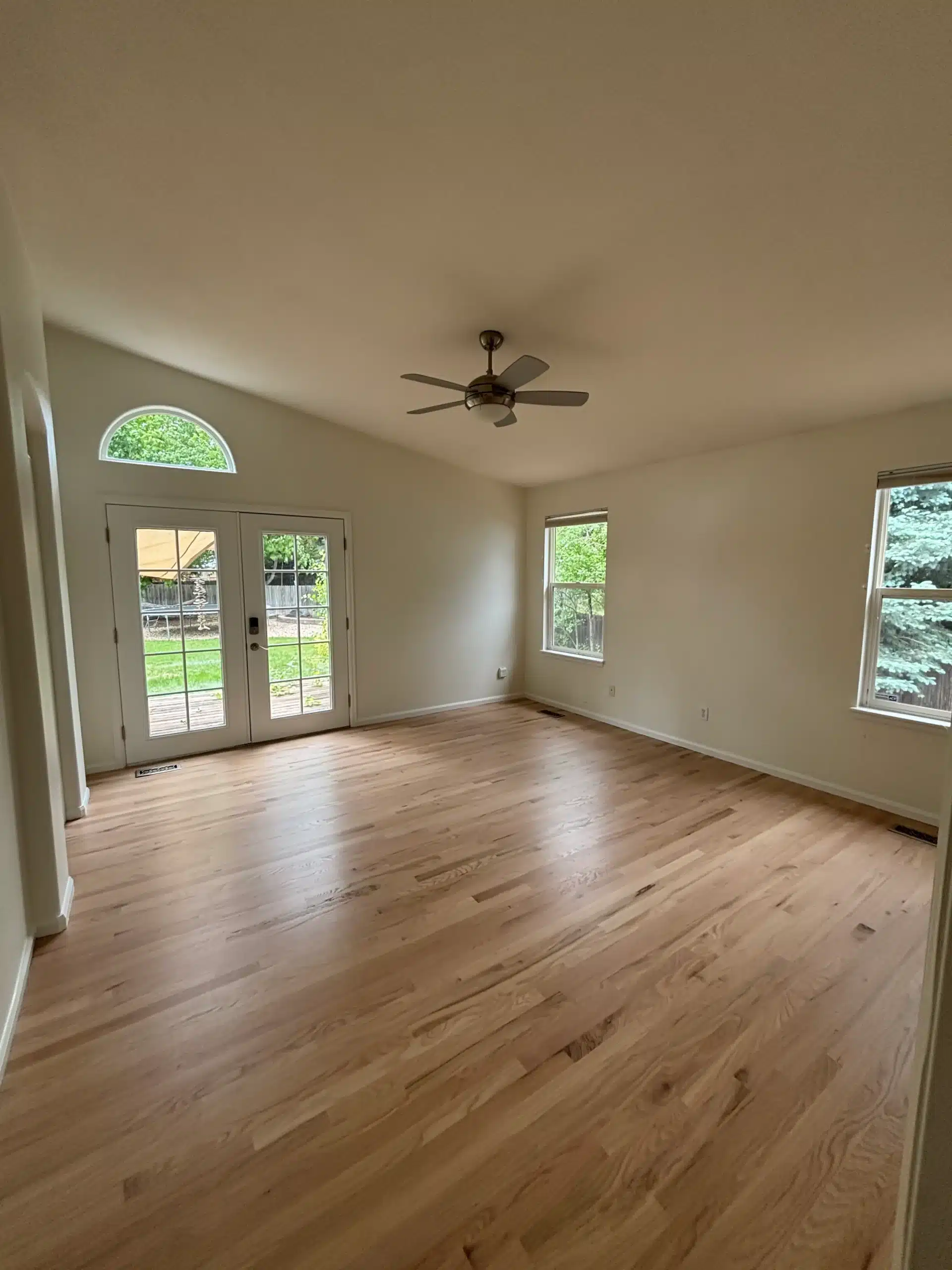 Spacious Bedroom with Light Walls and Hardwood A bright, empty bedroom featuring light neutral walls, gleaming hardwood floors, and multiple windows, perfect for residential painting projects.