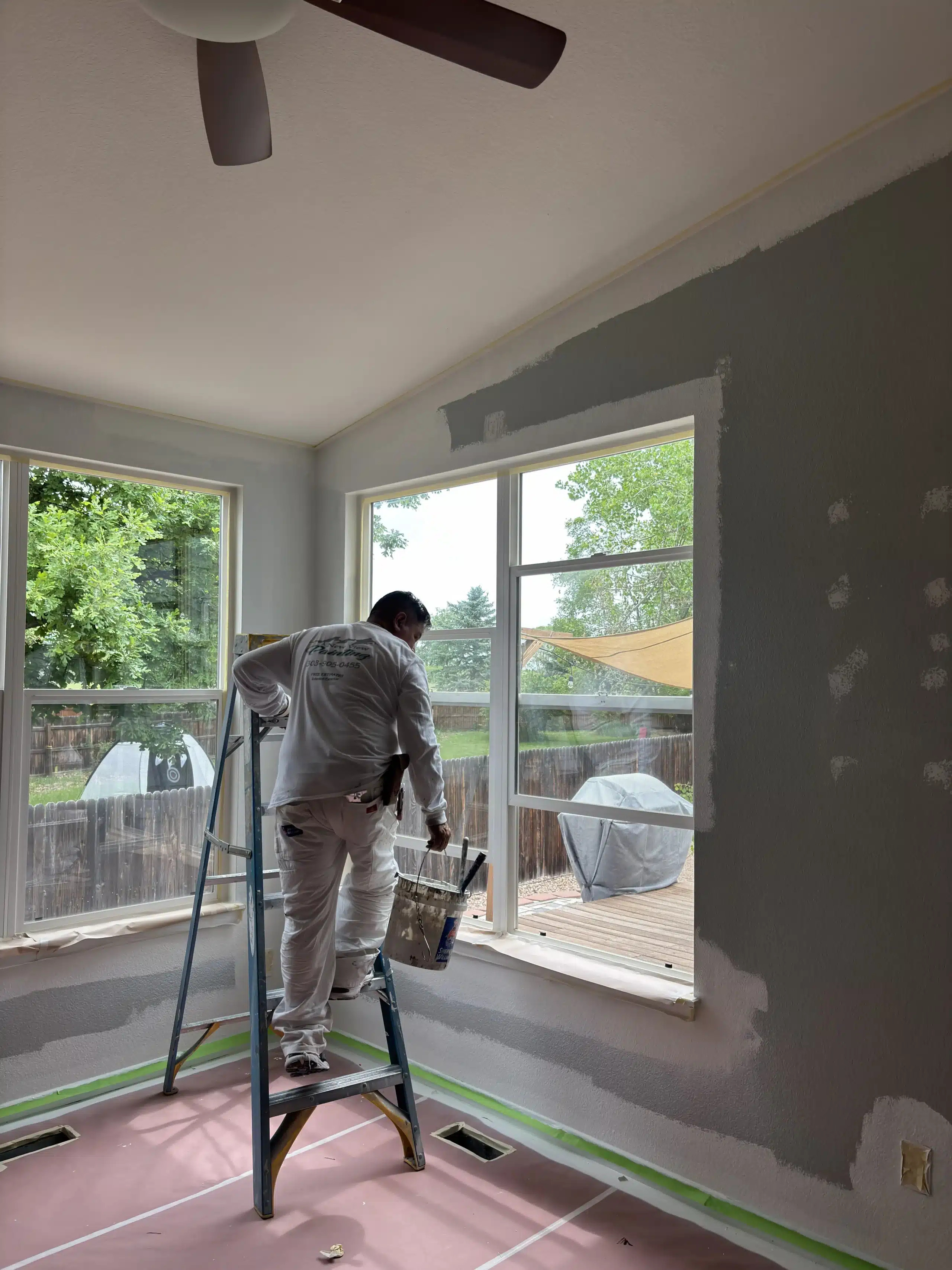 Residential Interior House Painting Services for a Sunroom A professional painter on a ladder meticulously paints interior walls and window trim of a residential sunroom.
