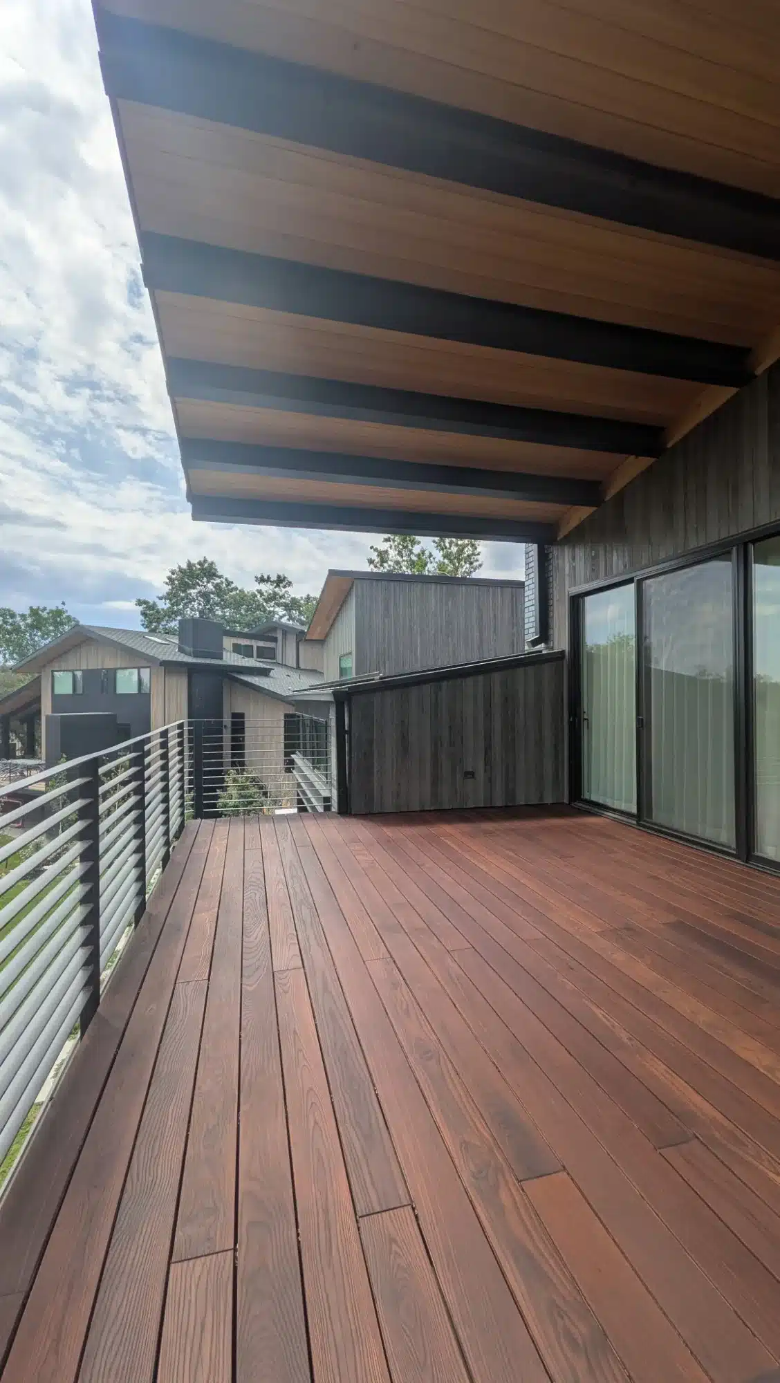 Modern Residential Deck With Wood Beams Reddish-brown stained composite deck with modern wood beam pergola, metal cable railing, and dark siding in Erie, Colorado