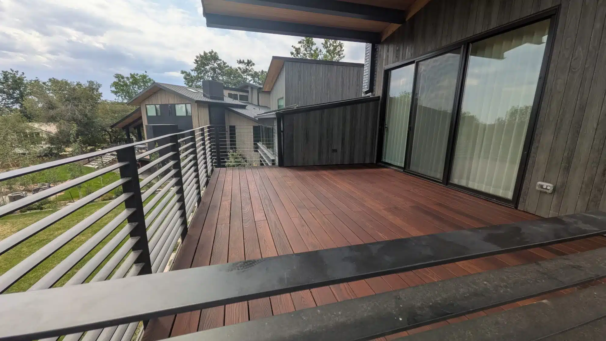 Reddish-Brown Composite Deck Stain Reddish-brown stained composite deck with black metal cable railing, dark wood siding, and modern residential roofline in