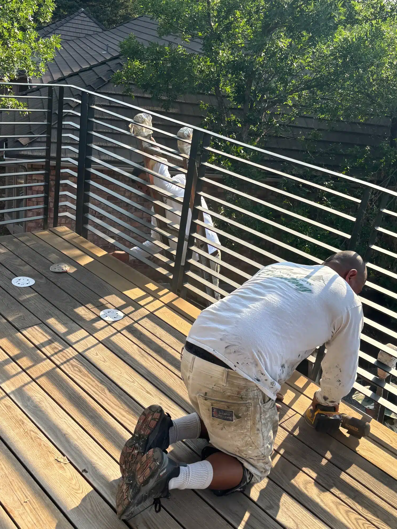 Residential Deck Staining Erie Colorado Painter applying stain to light wood deck boards with black horizontal metal railing and dark roof in background